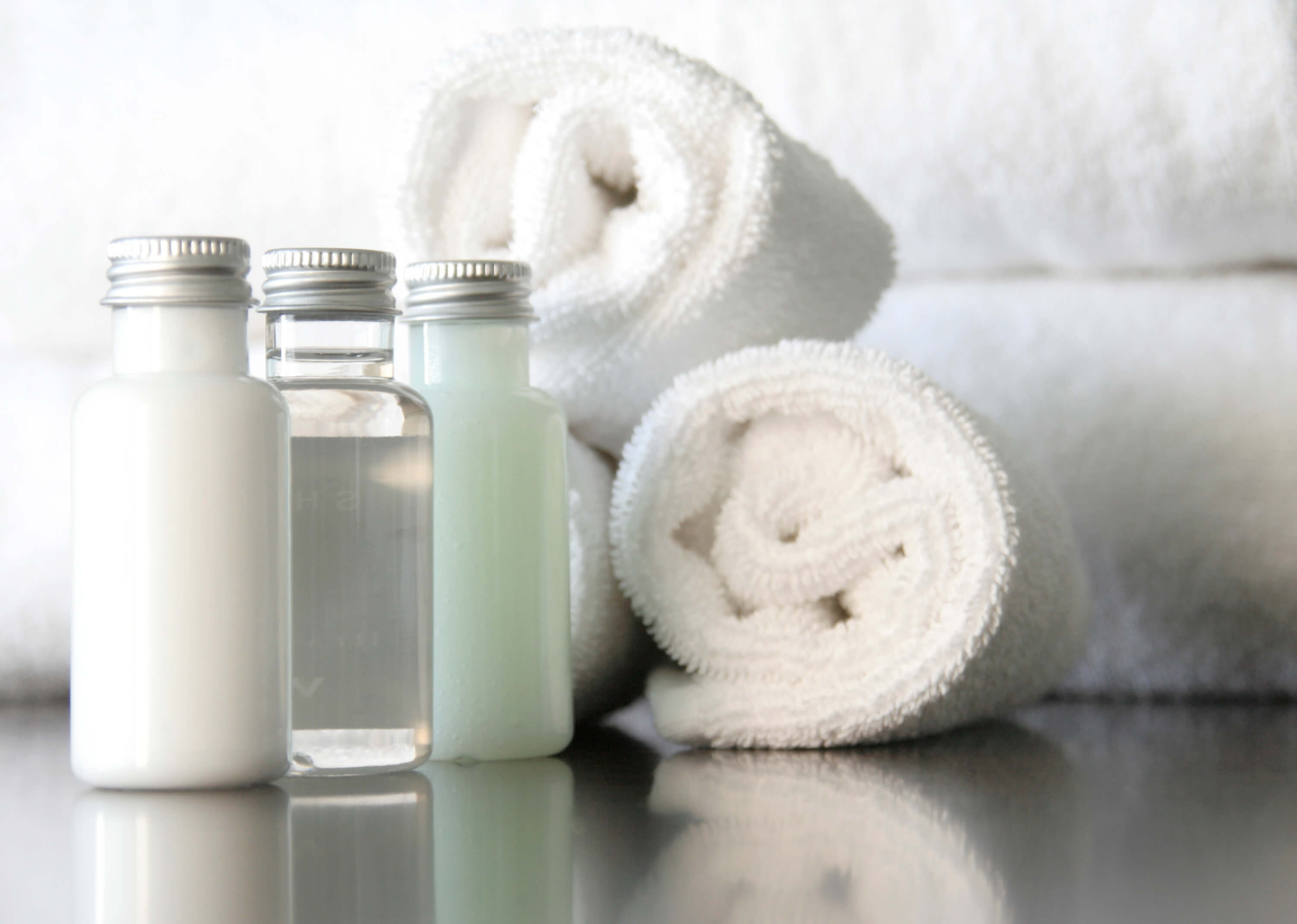 Close up of three bottles containing cosmetics against a background of rolled up white fluffy towels